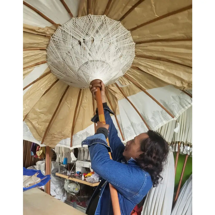 A white intricately woven paper umbrella with a wooden handle shown with an orange canvas bali patio parasol 2m