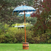 A vibrant turquoise canvas bali patio parasol with gold trim and tassels on a bamboo pole and wooden barrel base