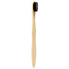 A light-colored bamboo toothbrush with medium soft black bristles made of charcoal material