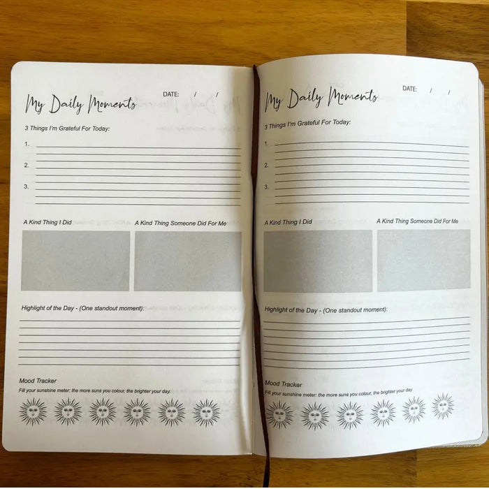 Open black gratitude journal with silver lining shows white pages with handwritten style text for daily gratitude and mood tracking