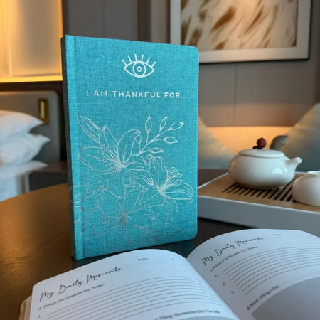 A blue gratitude journal with a turquoise linen cover embroidered with an eye and floral design and text i am thankful for