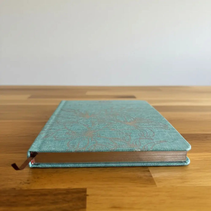 A blue gratitude journal with a teal textured cover and subtle silver floral pattern for daily thankfulness writing