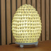 A warm glowing boho buting shell lamp shaped like a pinecone with a textured oval 15cm molded resin surface