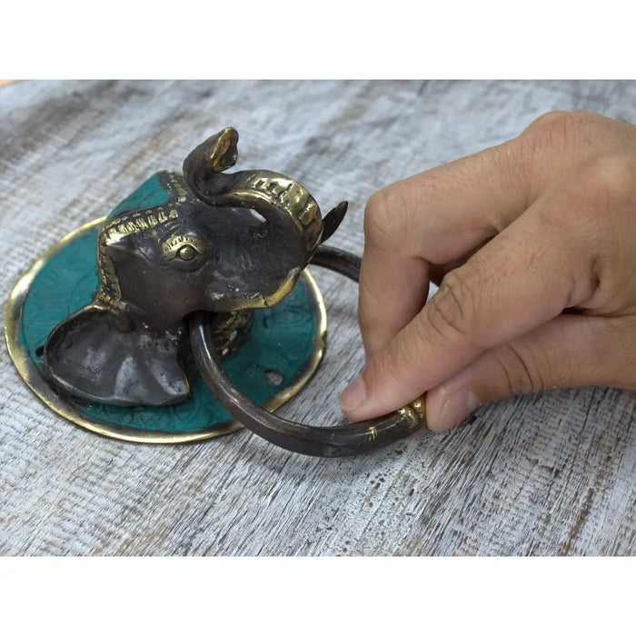 Antique brass door knocker shaped like an elephant head with turquoise inlay and a ring handle