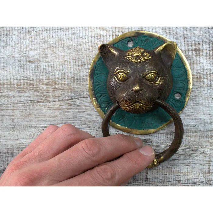 Brass door knocker with an antique bronze cat face design on a teal enamel background with gold accents