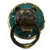 Brass door knocker shaped like an antique bronze and green enamel leopard head with gold accents on a wooden door
