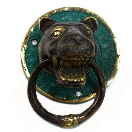 Brass door knocker shaped like an antique bronze and green enamel leopard head with gold accents on a wooden door