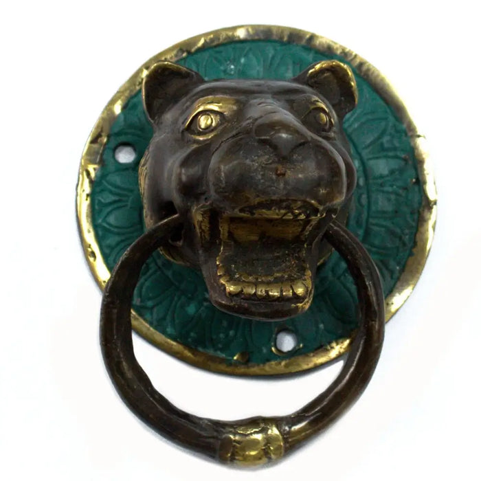 Brass door knocker shaped like an antique bronze and green enamel leopard head with gold accents on a wooden door