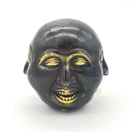 Black ceramic face ornament with gold painted eyes nose and teeth shown with a 10cm brass four face buddha