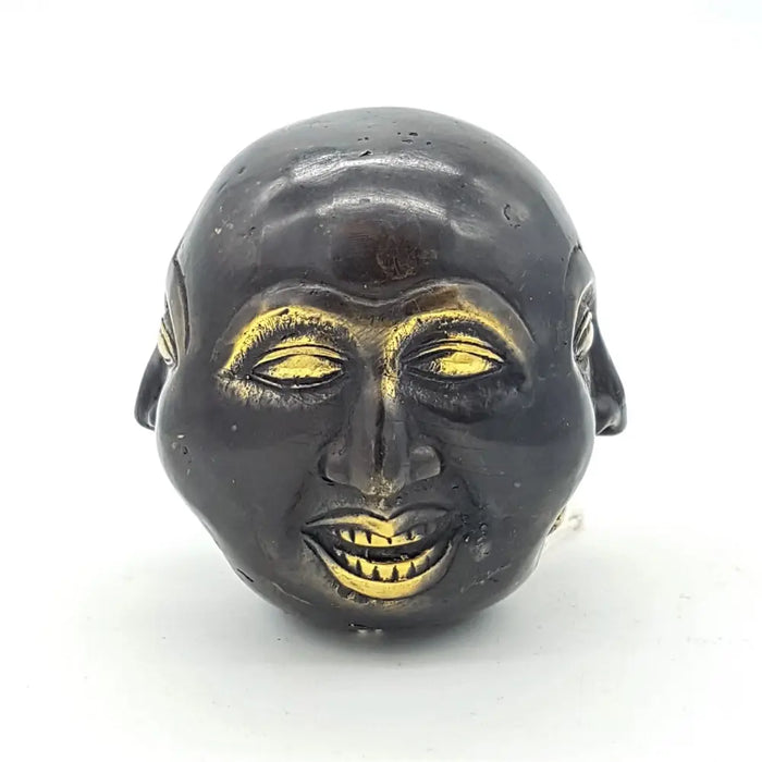Black ceramic face ornament with gold painted eyes nose and teeth shown with a 10cm brass four face buddha