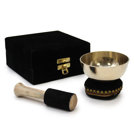 Shiny gold-toned brass singing bowl on black velvet base with ornate border and wooden mallet wrapped in black felt