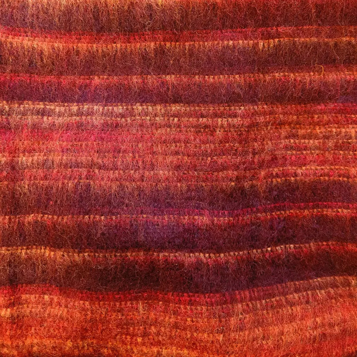 A textured hand-knitted scarf with horizontal stripes in red orange and burgundy shown with brushed cashmelon ali baba trousers