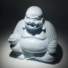 A white ceramic laughing buddha statue with sky blue crackle glaze seated in a meditative pose
