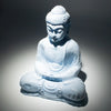 A white stone buddha glow lamp with a cracked texture seated in meditation in a sky blue setting
