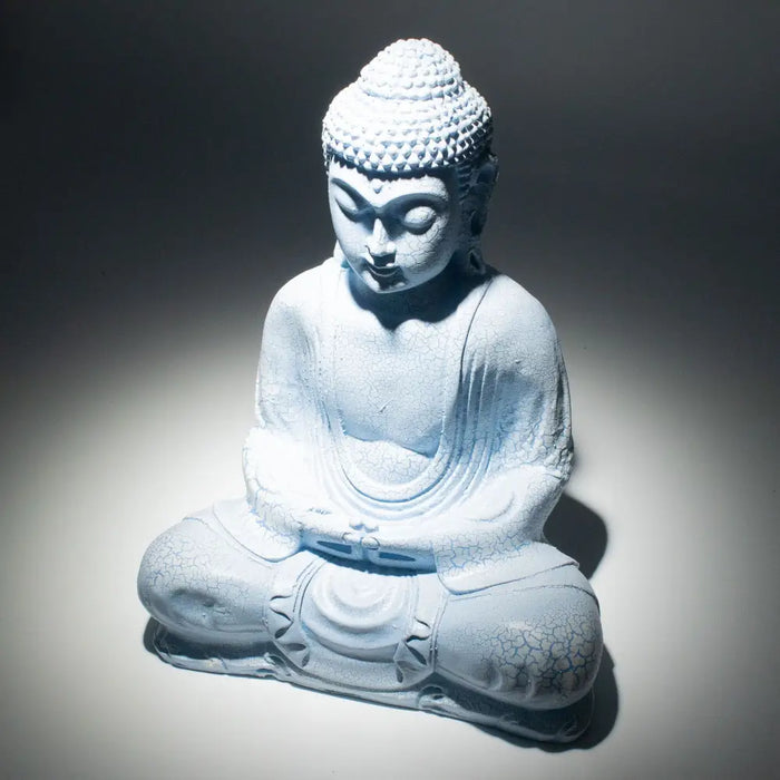 A white stone buddha glow lamp with a cracked texture seated in meditation in a sky blue setting