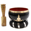 Black singing bowl set with gold rim and buddha silhouette resting on black cushion with silver stripes