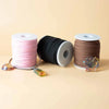 Three spools of bulk roll pendant cord in pink black and dark brown faux suede on a neutral surface