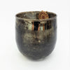 A burnished smoked glass votive candle holder with an etched bronze metallic finish and embossed grid texture