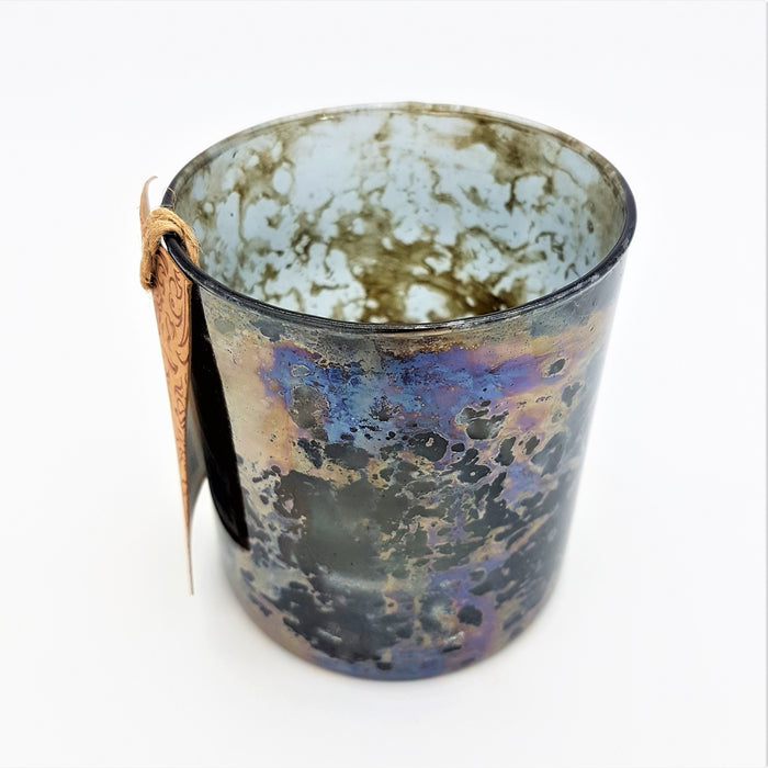A rustic burnished smoked glass votive with iridescent blues and purples in a mottled oil on water pattern