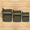 Three olive canvas laptop travel pouches with black zippers and white reflective stripes shown side by side
