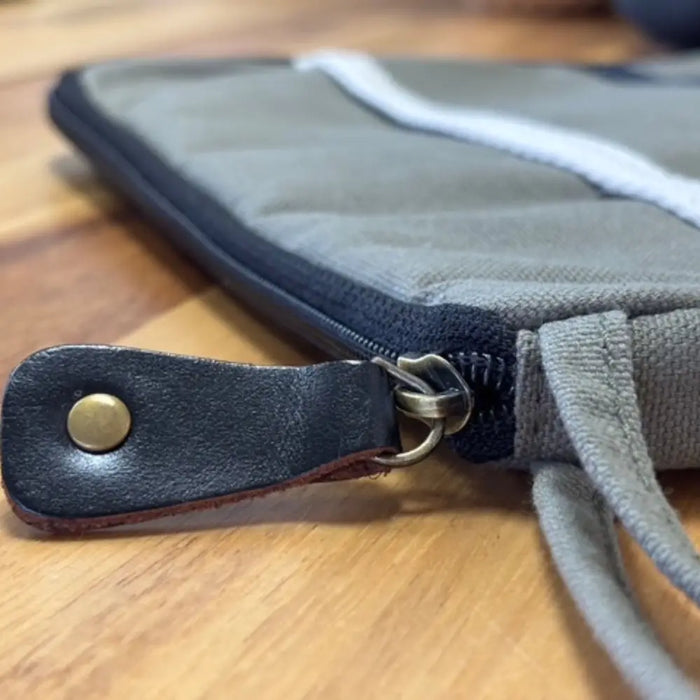 Gray canvas laptop travel pouch with black leather zipper pull and white stitching in olive tone