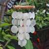 A capiz shell and driftwood crossed wind chime with white translucent oval discs hanging from natural wood
