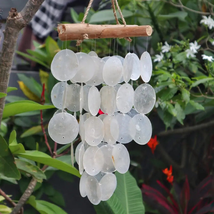 A capiz shell and driftwood crossed wind chime with white translucent oval discs hanging from natural wood