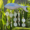 A rustic blue and white wooden fish wind chime with capiz shells and light wood beads hanging from its tail