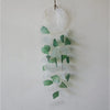 A capiz shell and glass wind chime with green and white translucent pieces hanging from a natural fiber cord