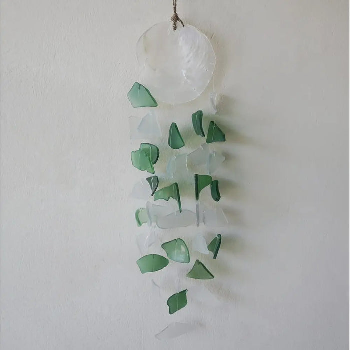 A capiz shell and glass wind chime with green and white translucent pieces hanging from a natural fiber cord