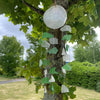 A capiz shell and glass wind chime with a circular top and green and white dangling fragments on thin strings