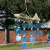 A handwoven beige raffia fish wind chime with blue capiz shells and white beads on five strings