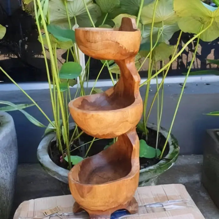 A three-tiered teak standing bowl fountain with smooth rounded edges and a natural light brown finish