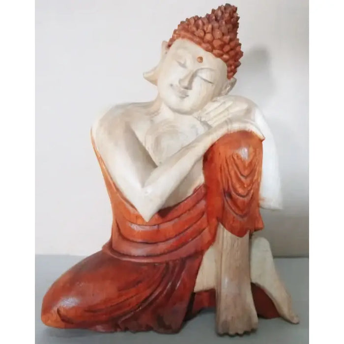 A serene carved wood buddha statue in orange red robes seated on a white base made from suar wood 25cm tall