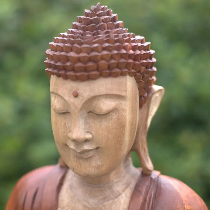 Carved wood buddha statue in natural suar wood with serene expression detailed spiked hair and red dot on forehead