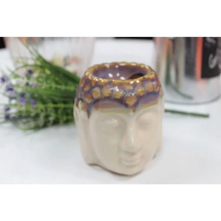 A ceramic oil burner shaped like a cream-colored buddha head with a glazed orange and purple decorative rim