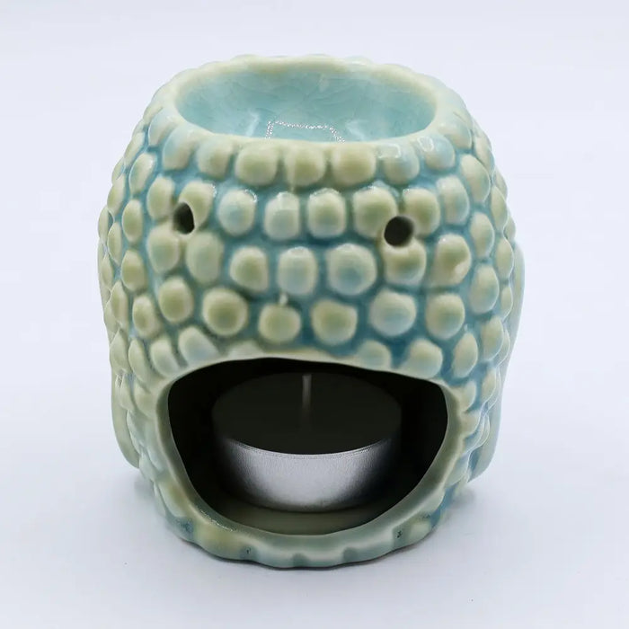 A pastel blue ceramic oil burner shaped like a smiling textured creature with small eye holes and rounded bumps