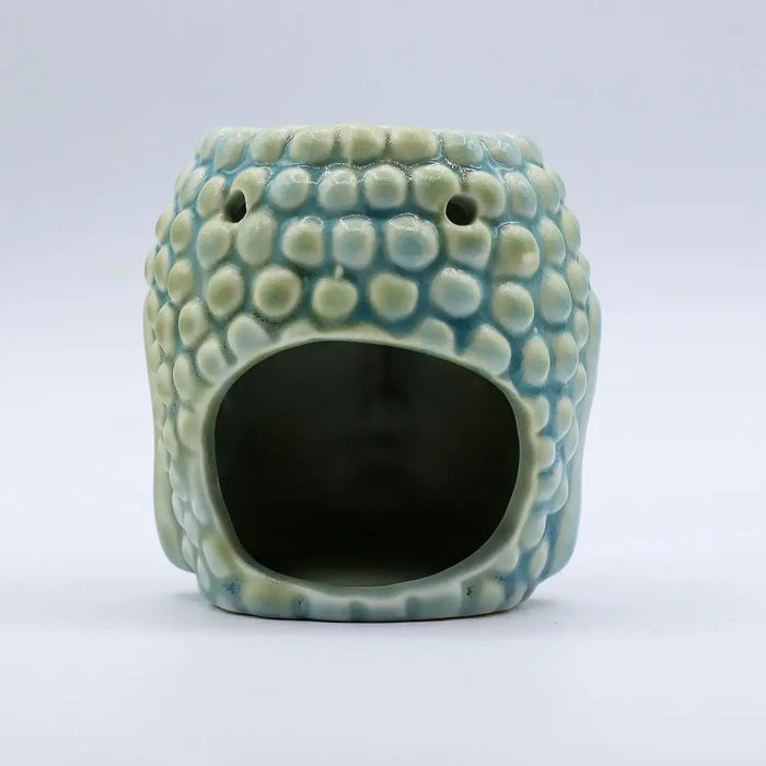 A pastel blue ceramic oil burner shaped like a buddha head with raised bumps and a textured glaze