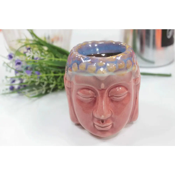 Pink ceramic oil burner shaped like a buddha head with a blue and gold glazed top rim in a simple setting