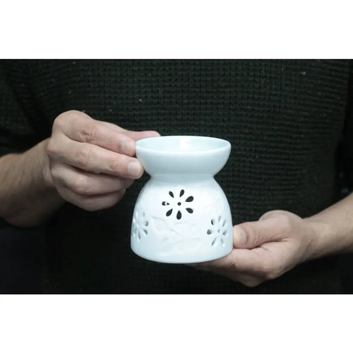 A white ceramic oil burner with floral cutout patterns and teal accents for home fragrance use