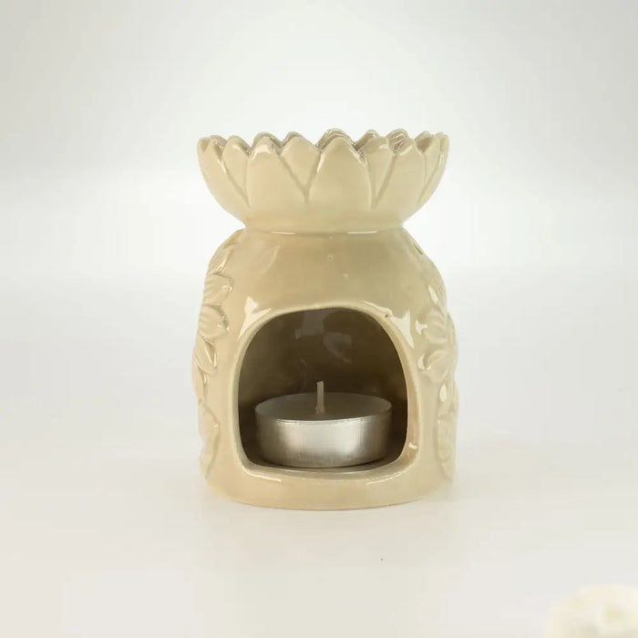 Cream-colored ceramic oil burner shaped like a lotus with carved floral pattern and silver tea light candle inside