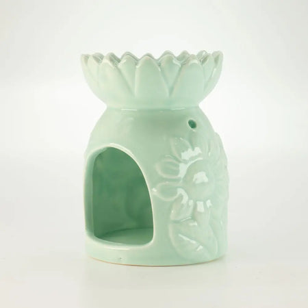 A pastel green ceramic oil burner shaped like a lotus flower with detailed floral relief and sunflower design