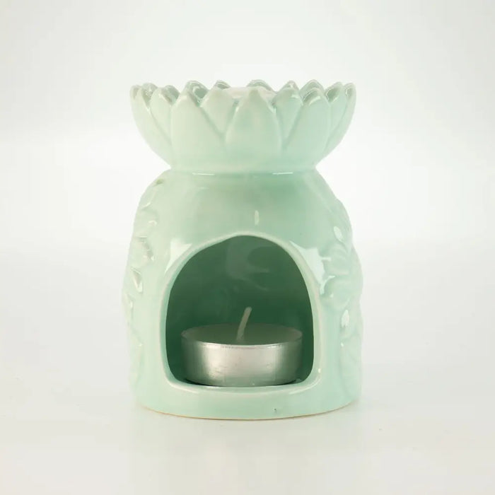 A pastel green ceramic oil burner shaped like a lotus flower with detailed petals and a silver tea light candle inside