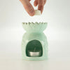 A pastel green ceramic oil burner shaped like a lotus with scalloped rim and textured sides holding a tealight candle