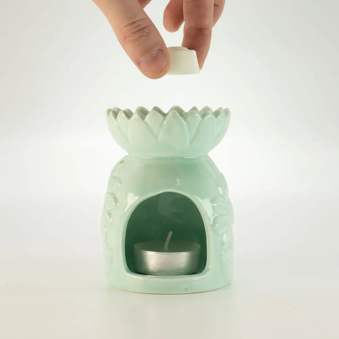 A pastel green ceramic oil burner shaped like a lotus with scalloped rim and textured sides holding a tealight candle