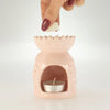 A pastel pink ceramic oil burner shaped like a lotus with detailed petals and a silver tea light inside