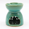 A teal ceramic oil burner with scalloped rim and white dots on front panel for burning essential oils