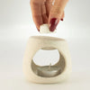 Cream-colored speckled ceramic oil burner zen pebble with circular cutout and silver tea light candle inside