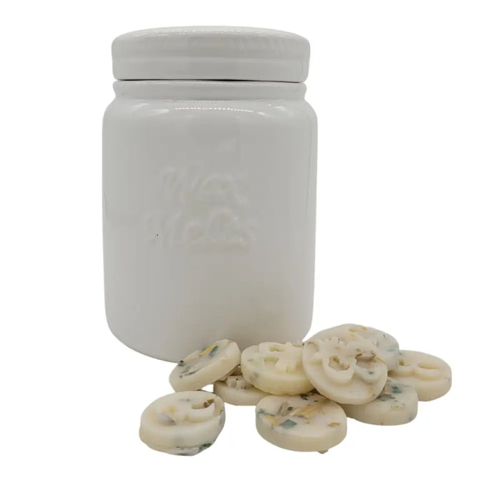 White ceramic storage jar with embossed logo filled with creamy off-white wax melts with dried botanicals
