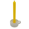 A vibrant yellow taper candle in a minimalist white ceramic tealight and dinner candle holder